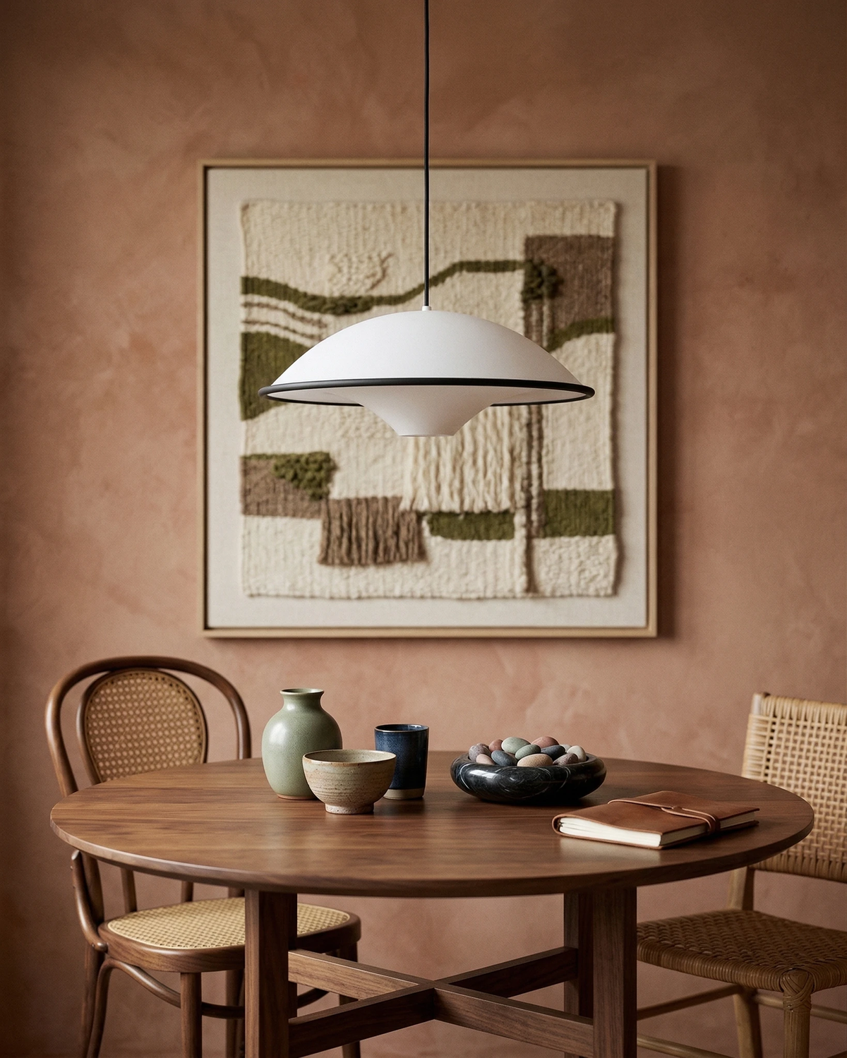 Acrylic pendant light AOSTA No.01 lit over a round wooden dining table with cane chairs and a terracotta wall