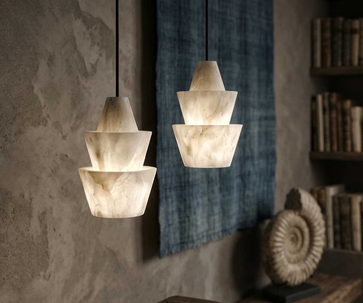 Two alabaster pendant lights ALABA No.06 glowing beside an indigo textile and an ammonite fossil on a plaster wall