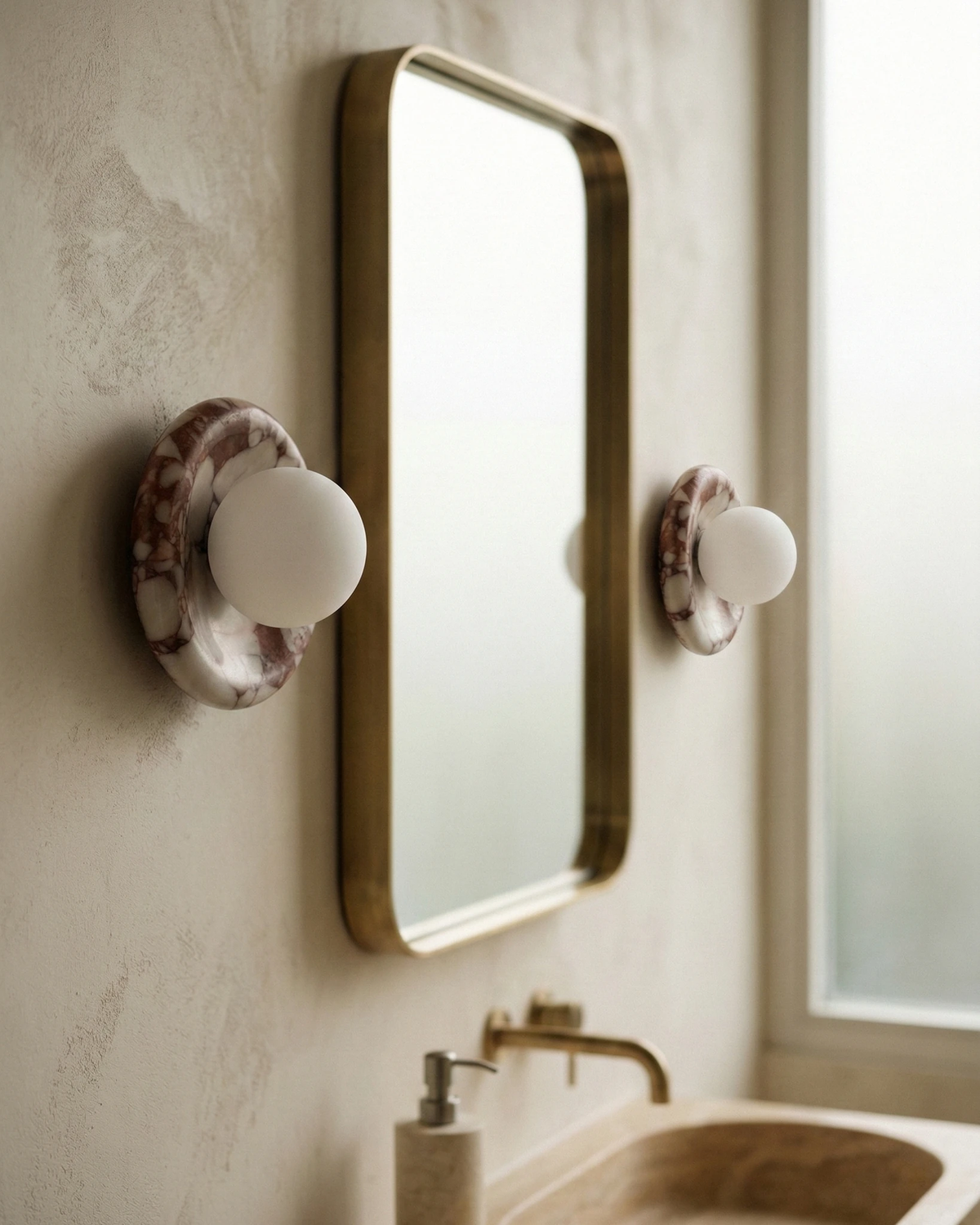 Two alabaster wall sconces LATTE No.02 in violet-veined stone beside a brass mirror above a stone sink, unlit