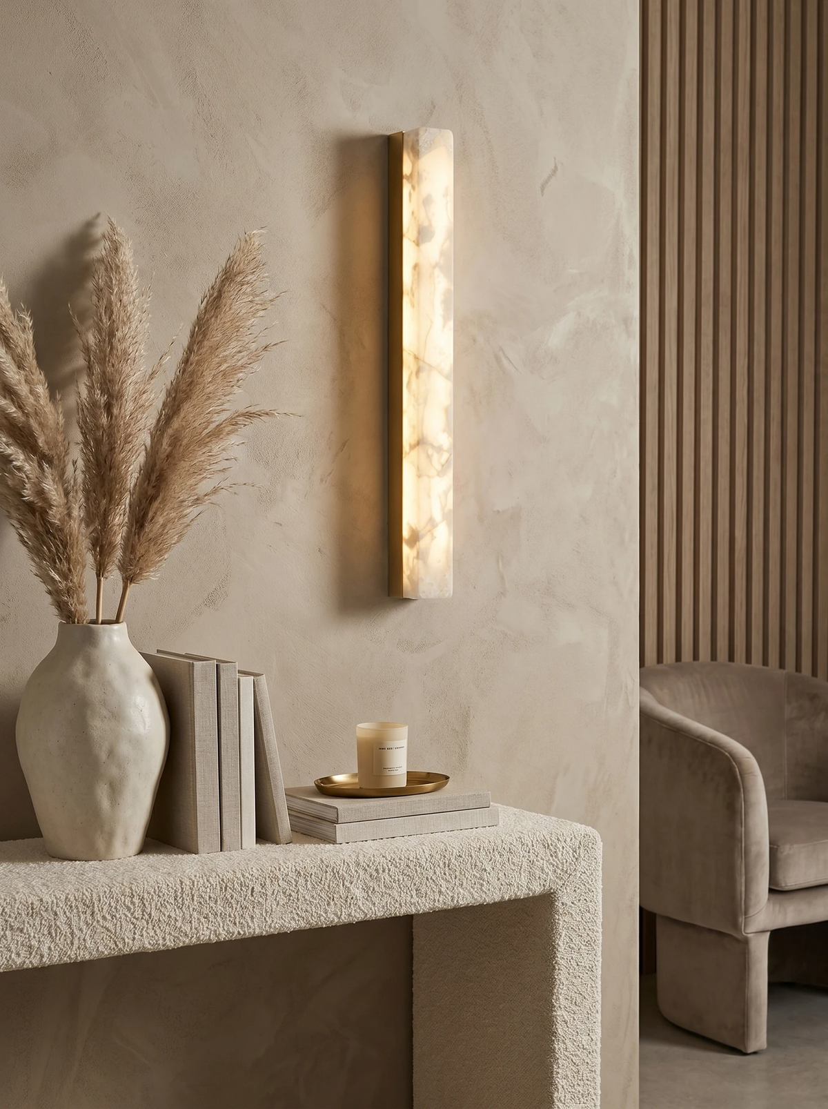 Alabaster wall sconce NEBBIA No.02 on a brass bar, lit above a boucle console with pampas grass and books