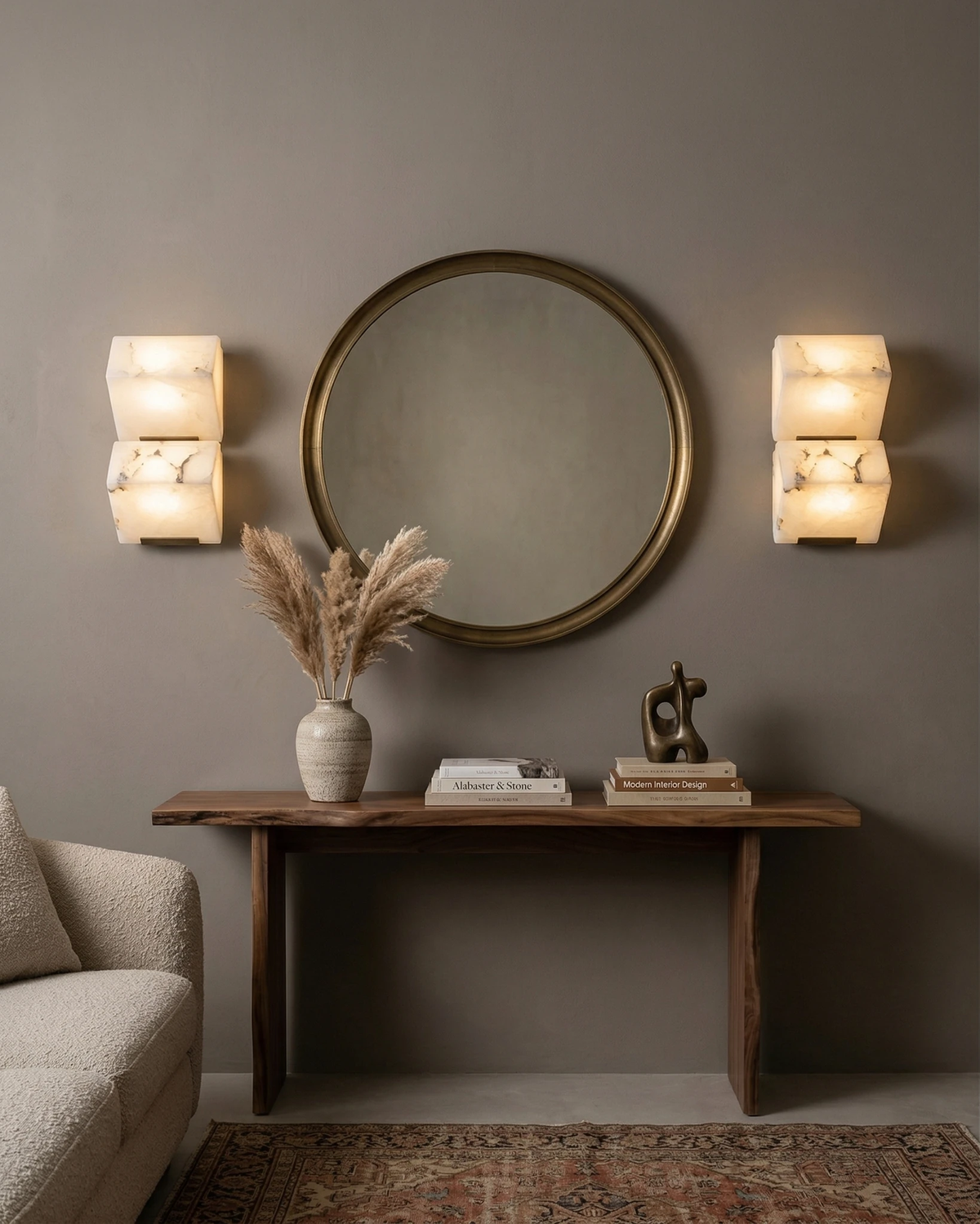 Two alabaster wall sconces ALABA No.05 duo lit beside a round brass mirror above a wooden console table