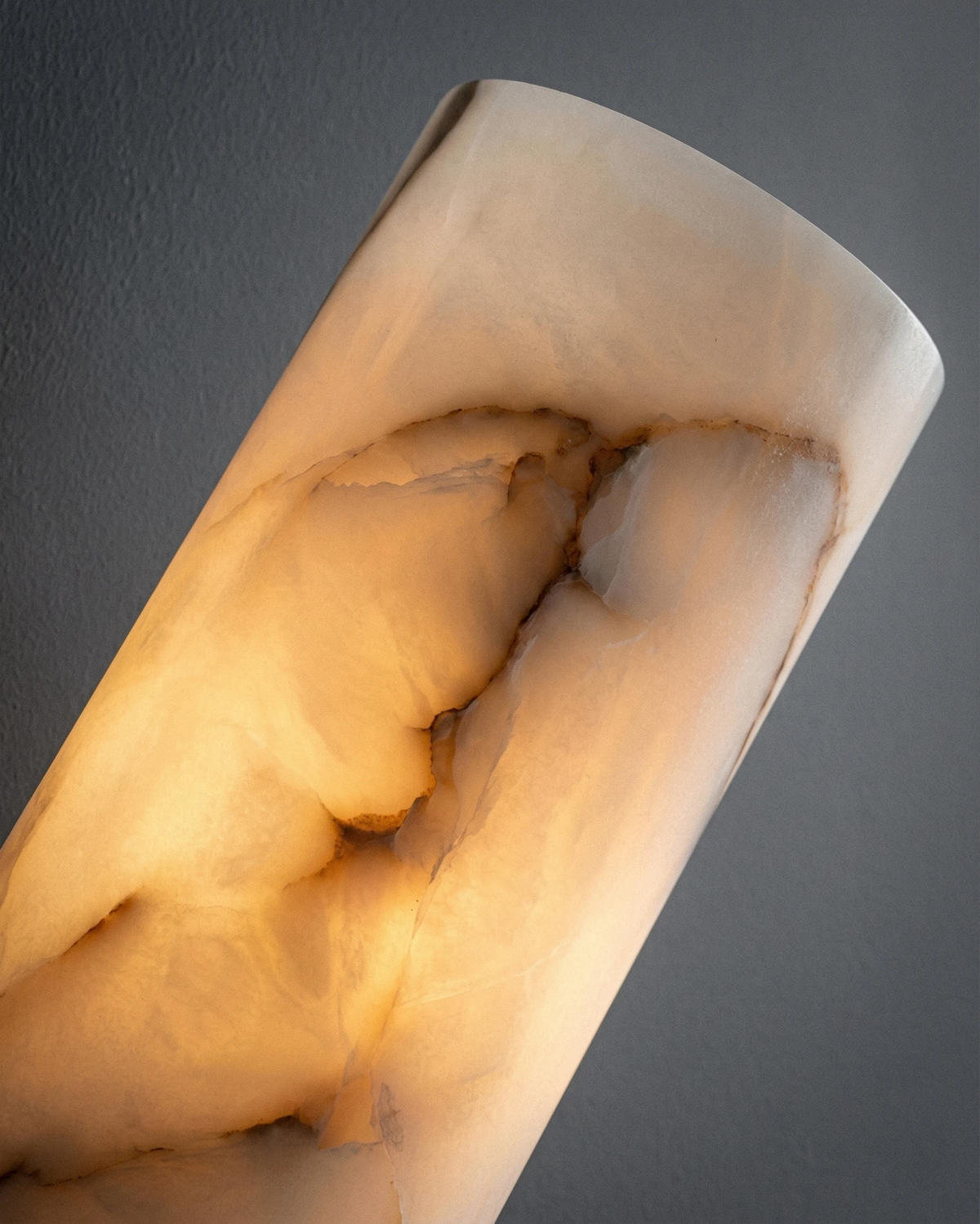 Close-up of the lit cream alabaster cylinder with gray veining on the ALABA No.07 alabaster wall sconce