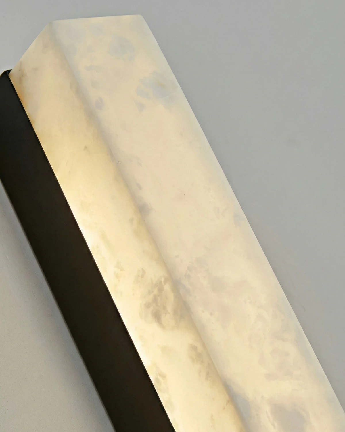 Close-up of the NEBBIA No.02 alabaster wall sconce, veined column glowing on a Volcano Black bar