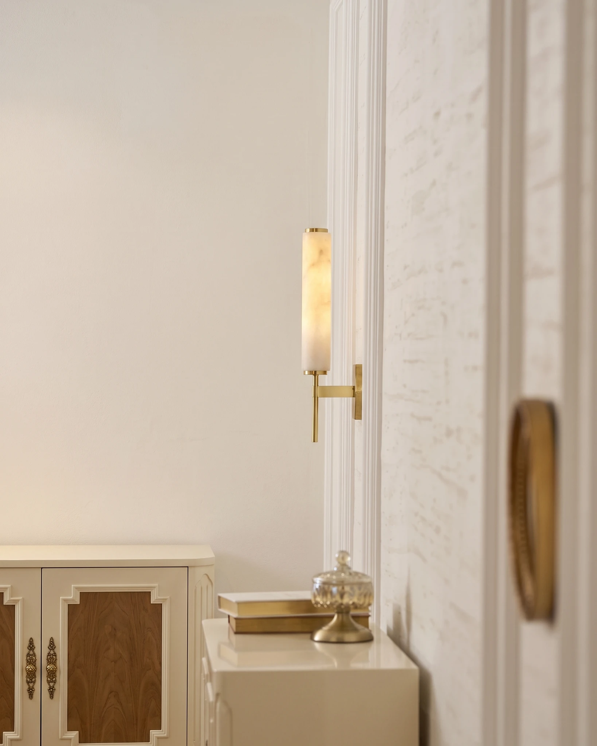 Alabaster wall sconce ALABA No.01 in brass lit beside a white cabinet in an entryway