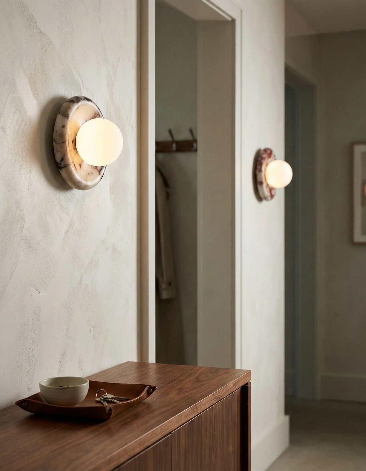 Alabaster wall sconce LATTE No.02 lit on a plaster entryway wall above a walnut console, mirrored by a second unit