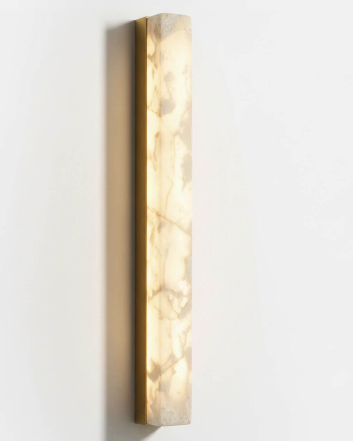 Alabaster wall sconce NEBBIA No.02, 40 in column on a brass bar, lit, seen at a slight angle on a white wall