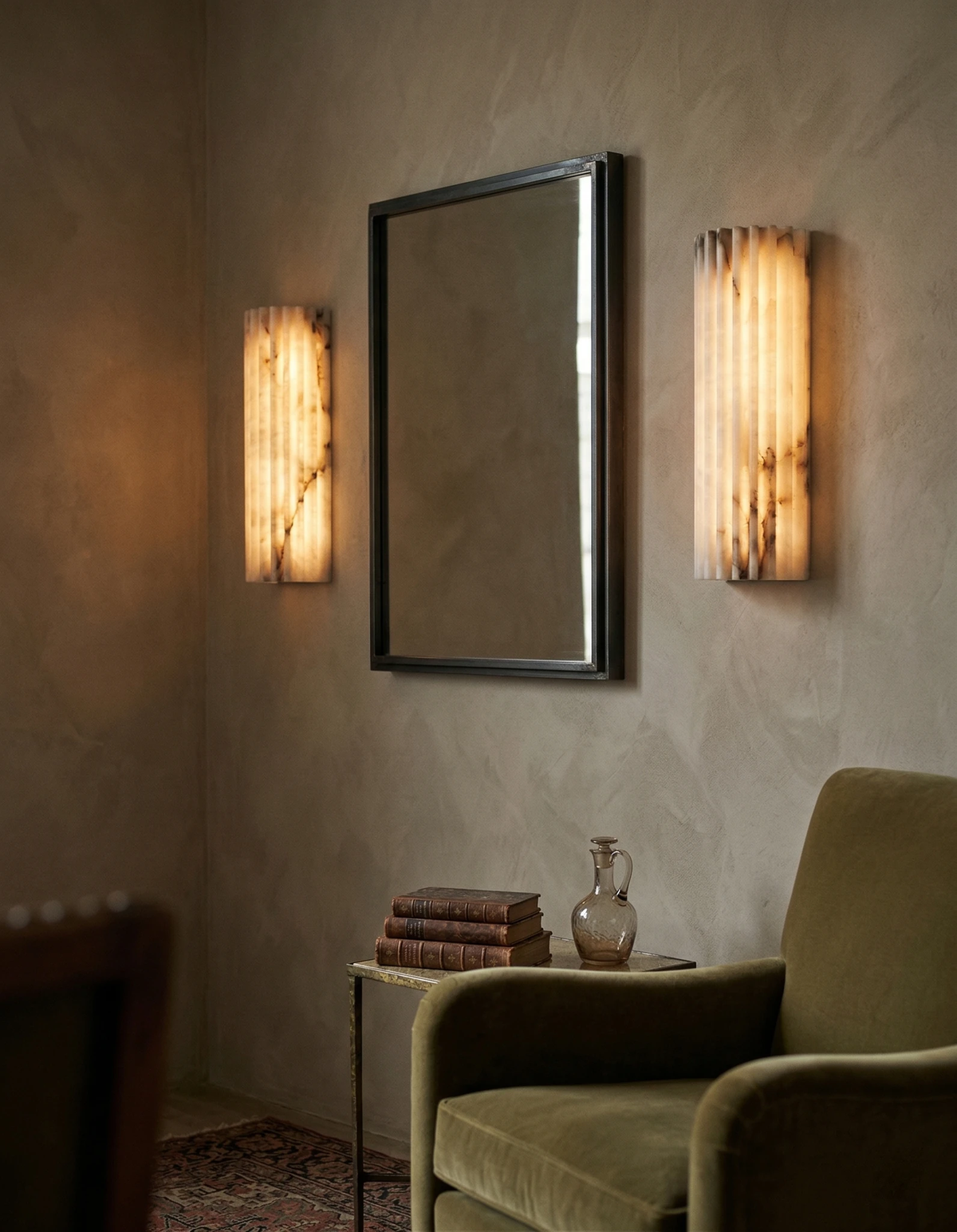Alabaster wall sconce ALABA No.02, a lit pair flanking a framed mirror above an olive velvet armchair in a living room