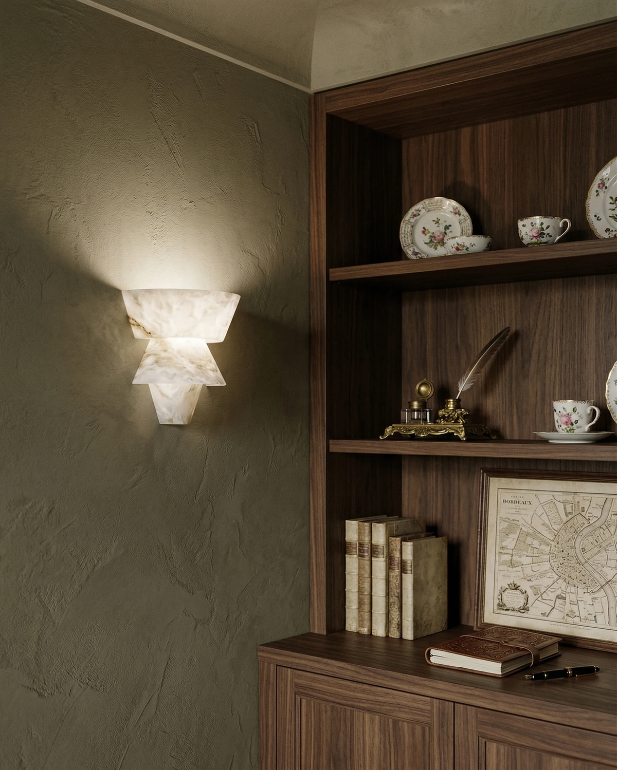 Alabaster wall sconce ALABA No.04 lit on a green plaster wall beside a walnut cabinet with shelves of books and plates