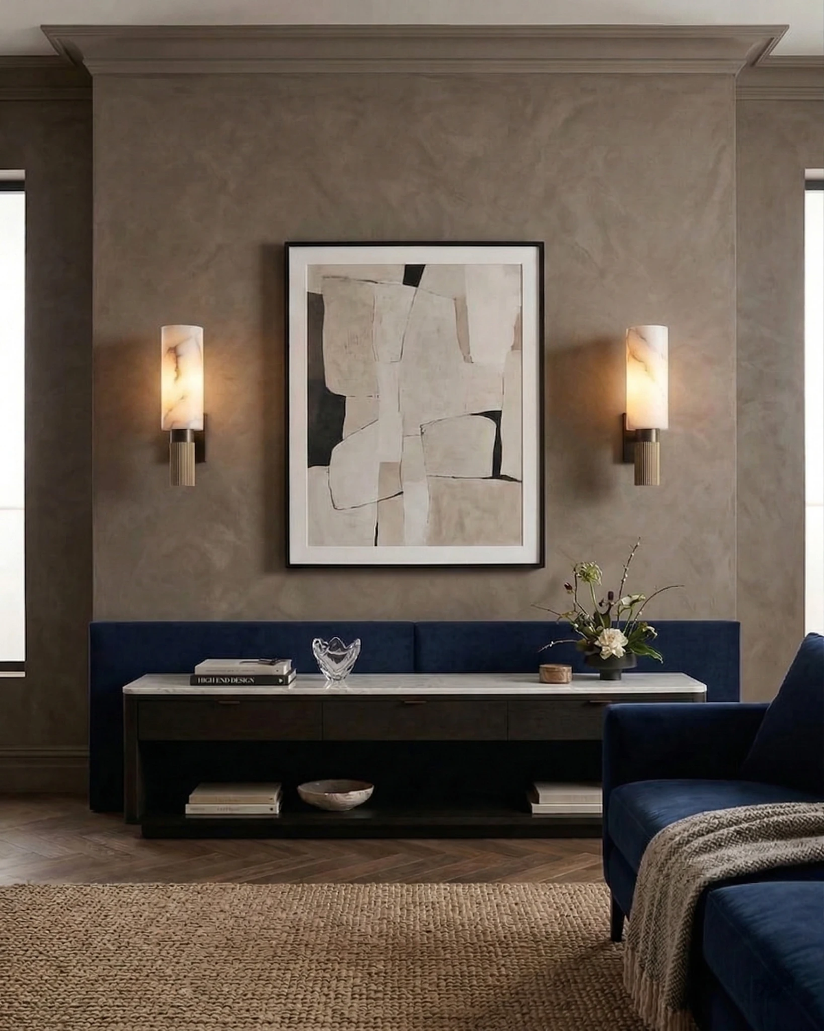 Pair of alabaster wall sconces ALABA No.07 lit either side of abstract art above a navy sofa in a plaster room
