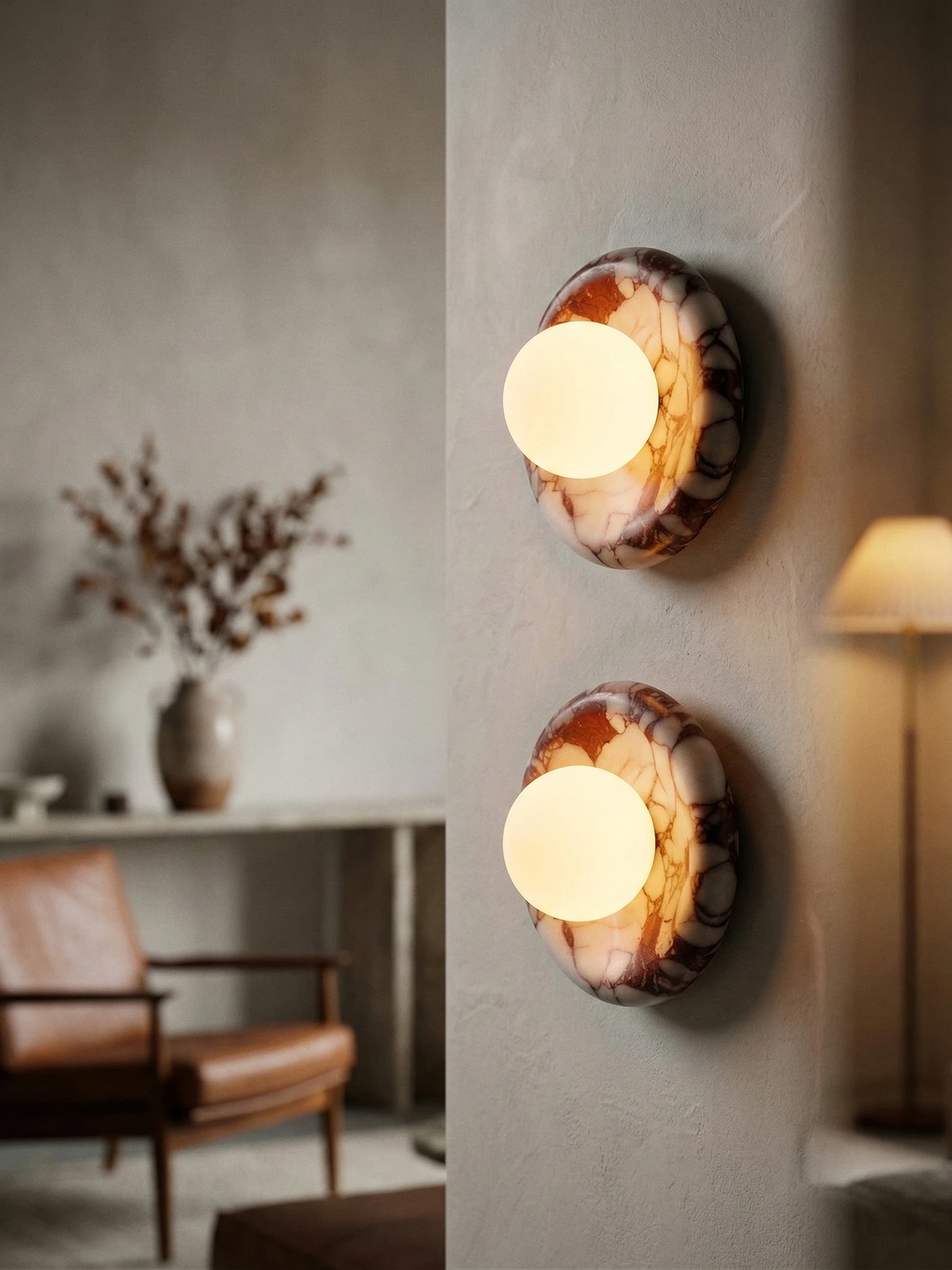 Two alabaster wall sconces LATTE No.02 with red-veined stone rings stacked and lit on a plaster column in a living room