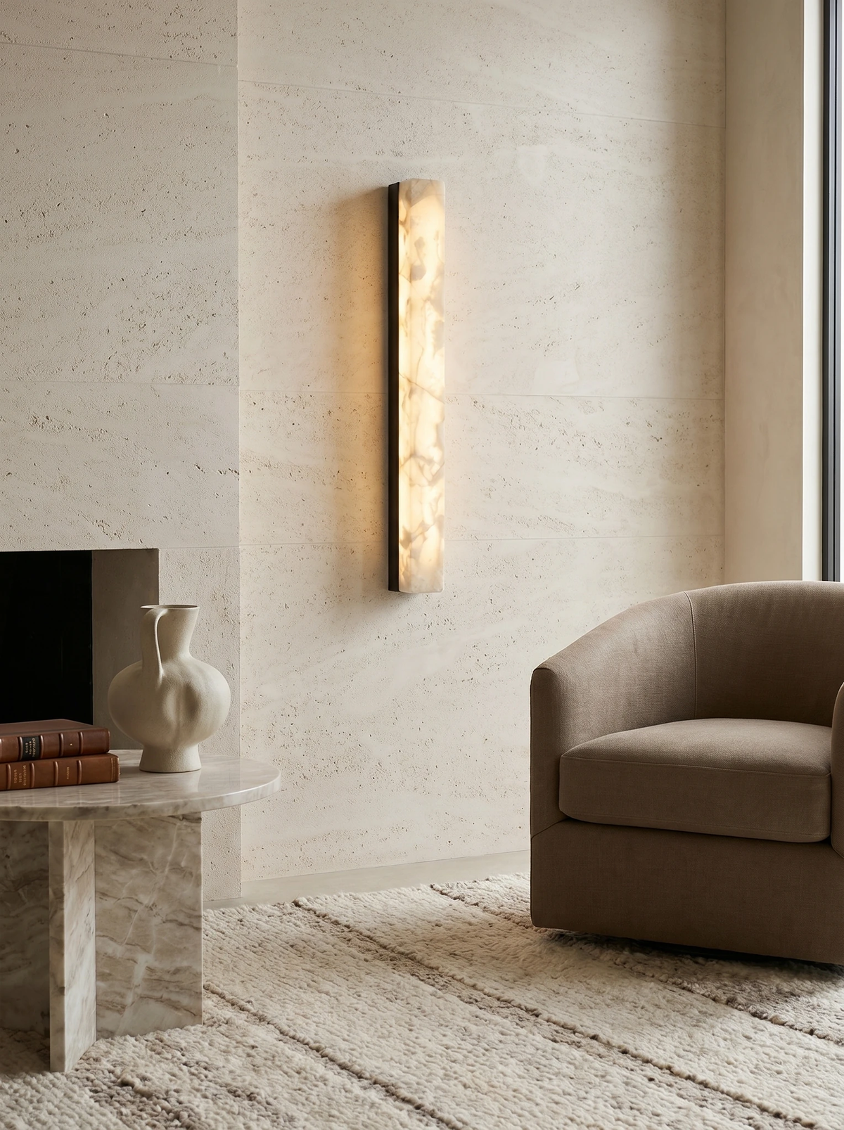 Alabaster wall sconce NEBBIA No.02 lit on a stone-clad wall beside a window, armchair and coffee table on a rug