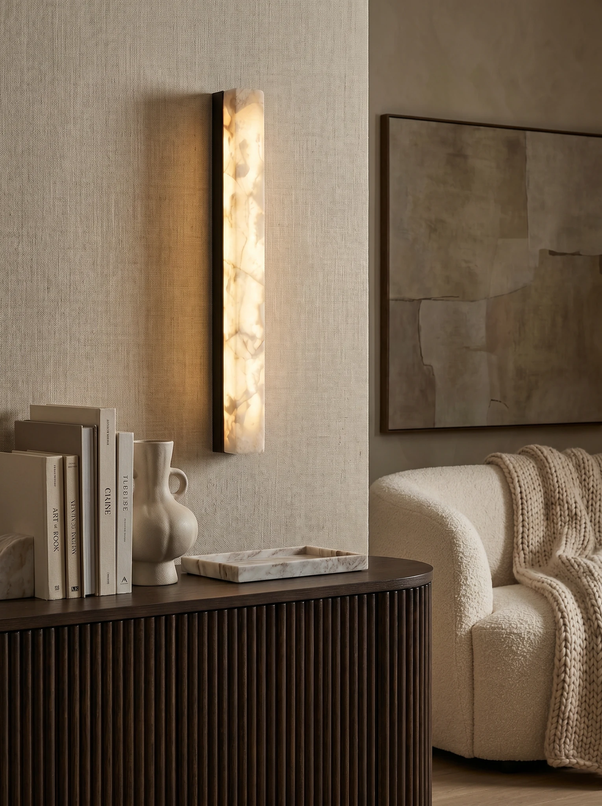 Alabaster wall sconce NEBBIA No.02 with black bar, switched on above a fluted wood sideboard with books and a boucle sofa