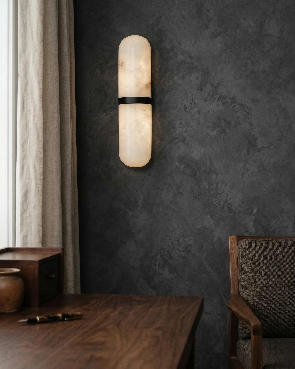 Alabaster wall sconce OLIVA No.01 with black band lit on a dark plaster wall above a walnut desk and chair