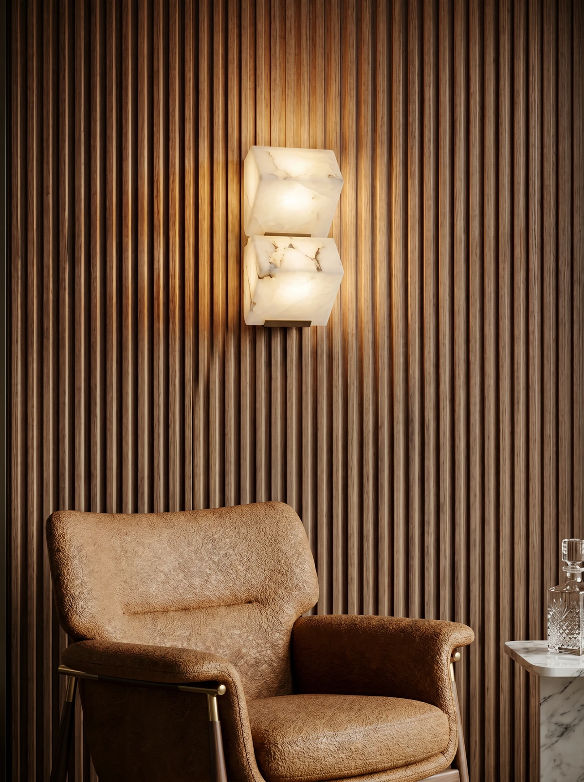 Alabaster wall sconce ALABA No.05 duo, two faceted blocks lit on a fluted wood wall above a tan leather armchair