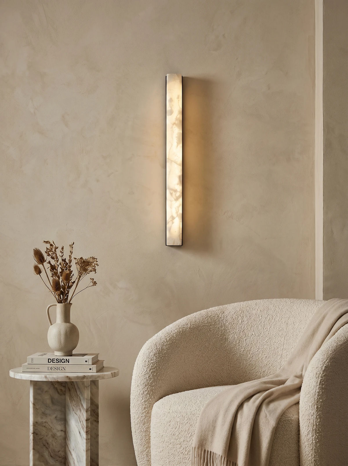 Alabaster wall sconce NEBBIA No.02 switched on above a boucle armchair and a stone side table with dried flowers