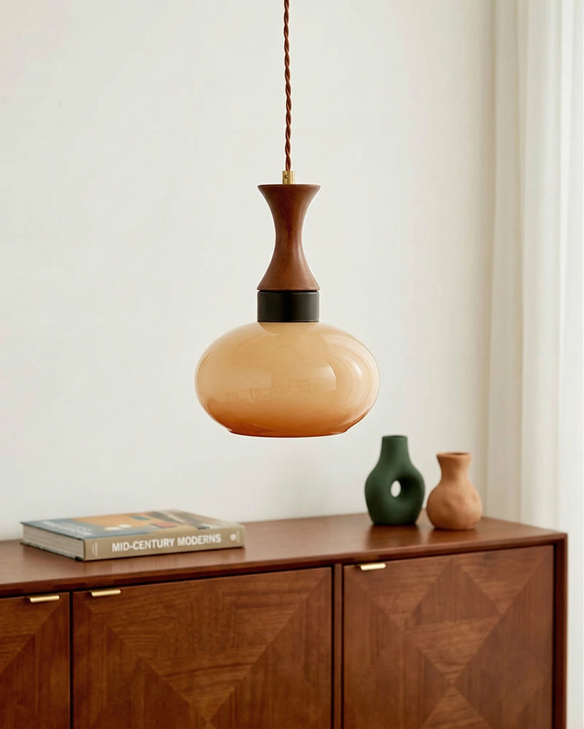 Amber glass pendant light OVIA No.04, amber disc on a walnut stem above a walnut sideboard with a vase