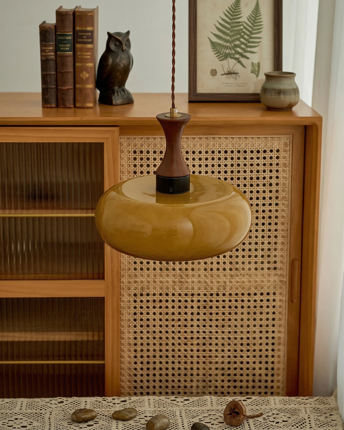 Amber glass pendant light OVIA No.04, disc shade in front of a rattan cabinet topped with books