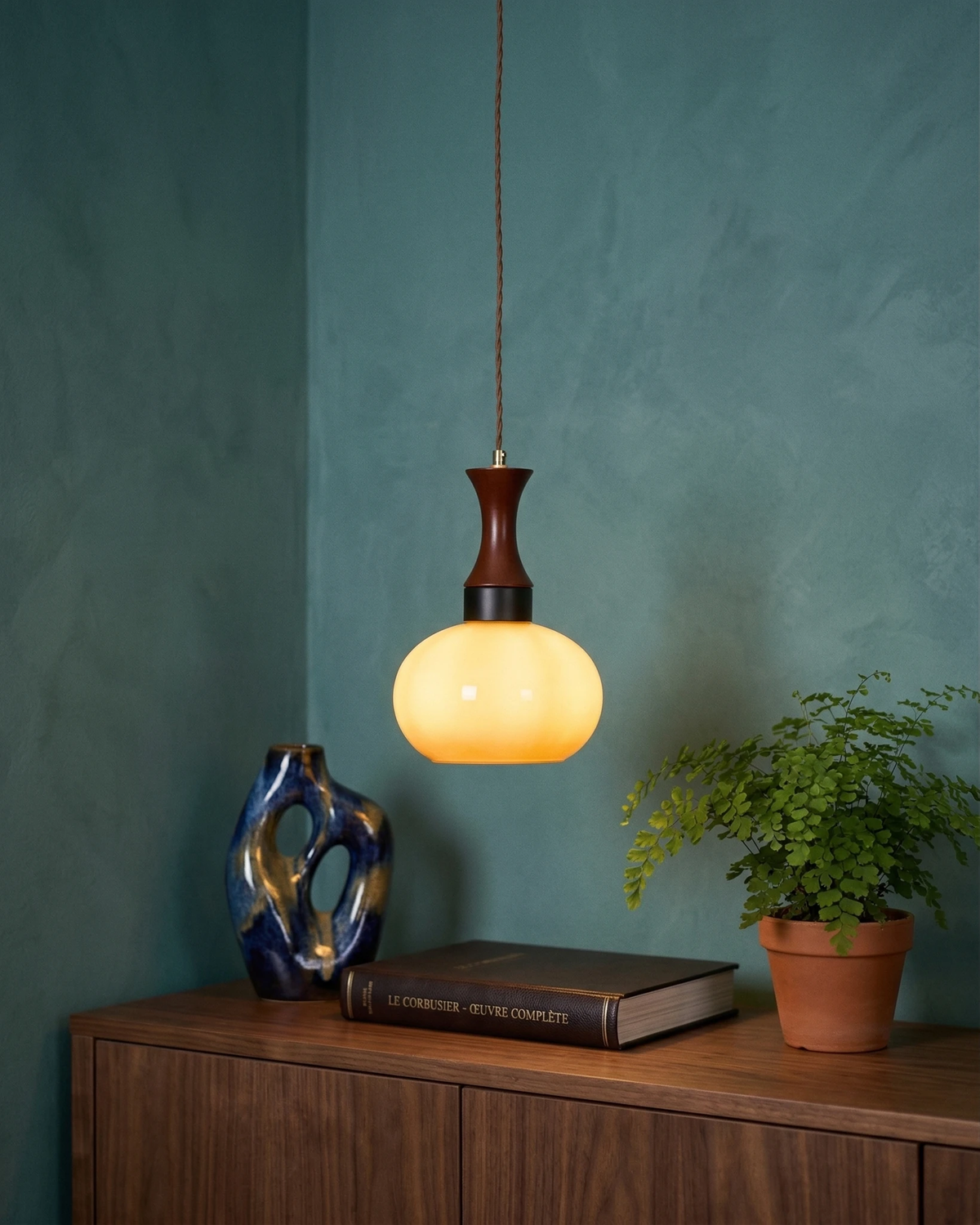 Amber glass pendant light OVIA No.04, dome shade glowing above a walnut sideboard on a teal wall