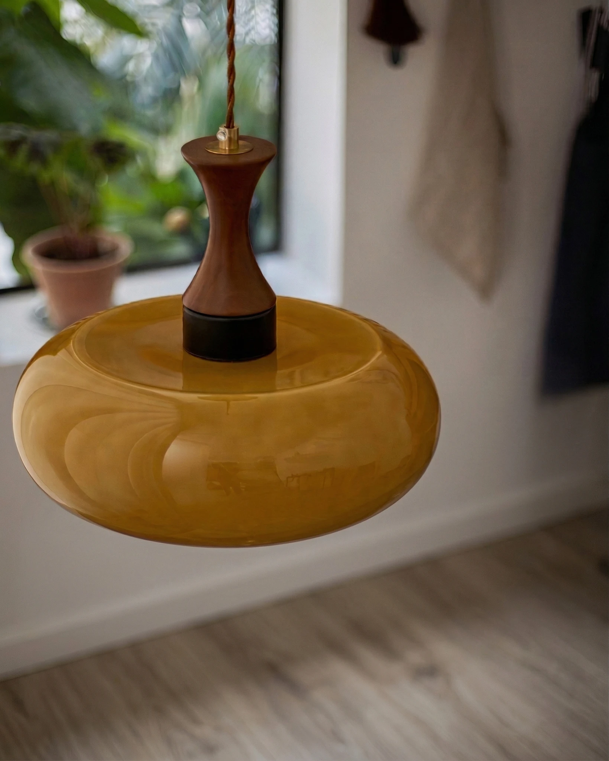 Close-up of the amber disc shade and walnut stem of the OVIA No.04 pendant, unlit, beside a window