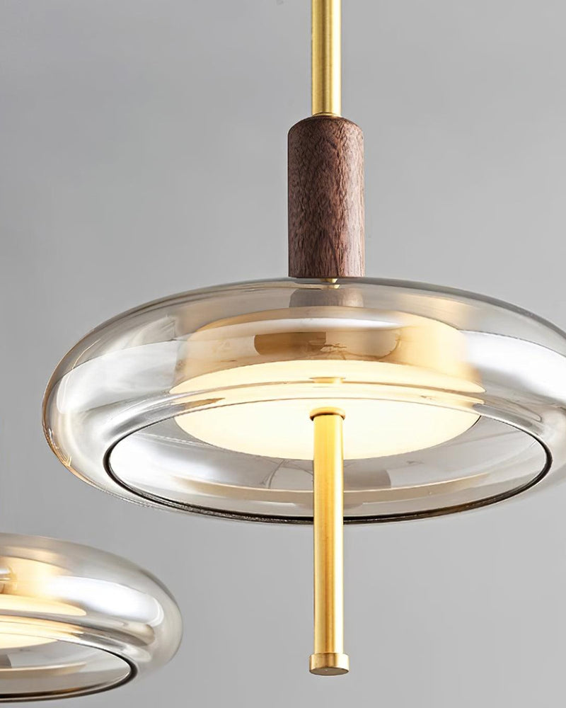Close-up of two lit NOCE No.01 amber glass pendant light discs with brass rods passing through the glass