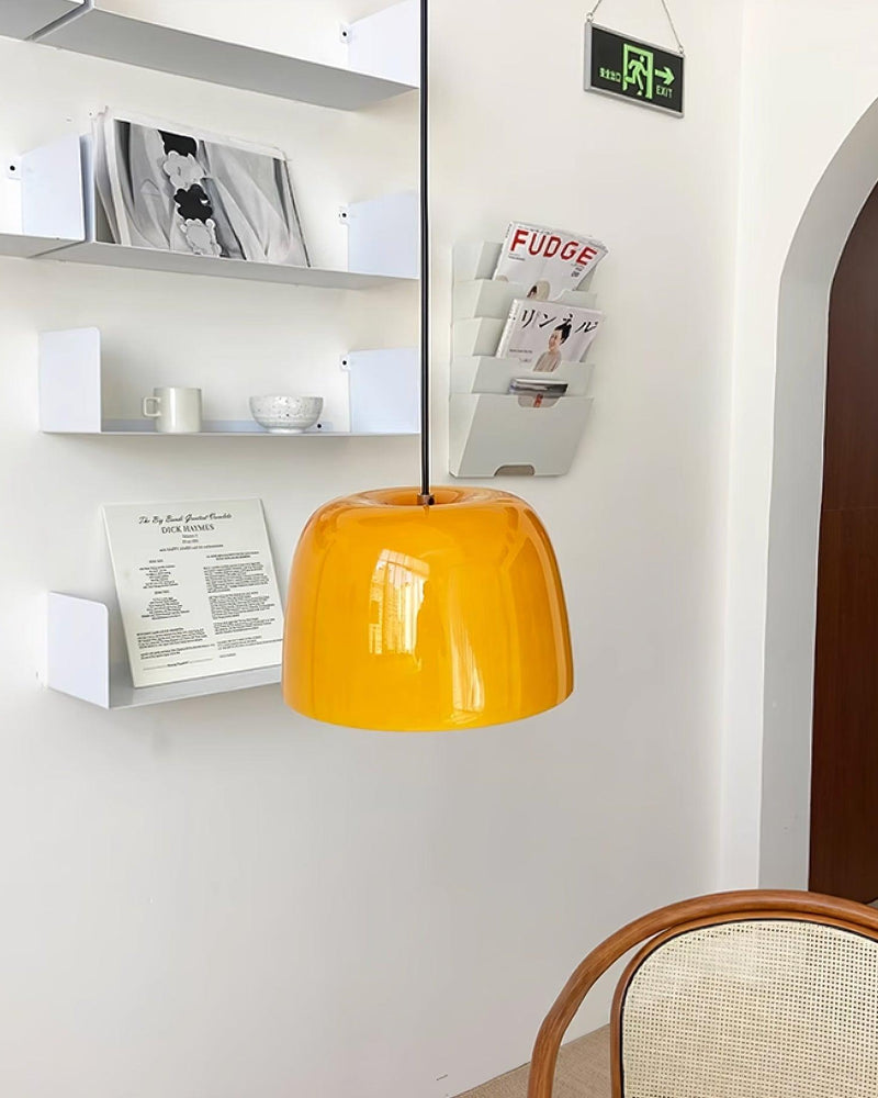 Amber glass pendant light MIELE No.01 hanging in a cafe with white wall racks of magazines and a bentwood chair