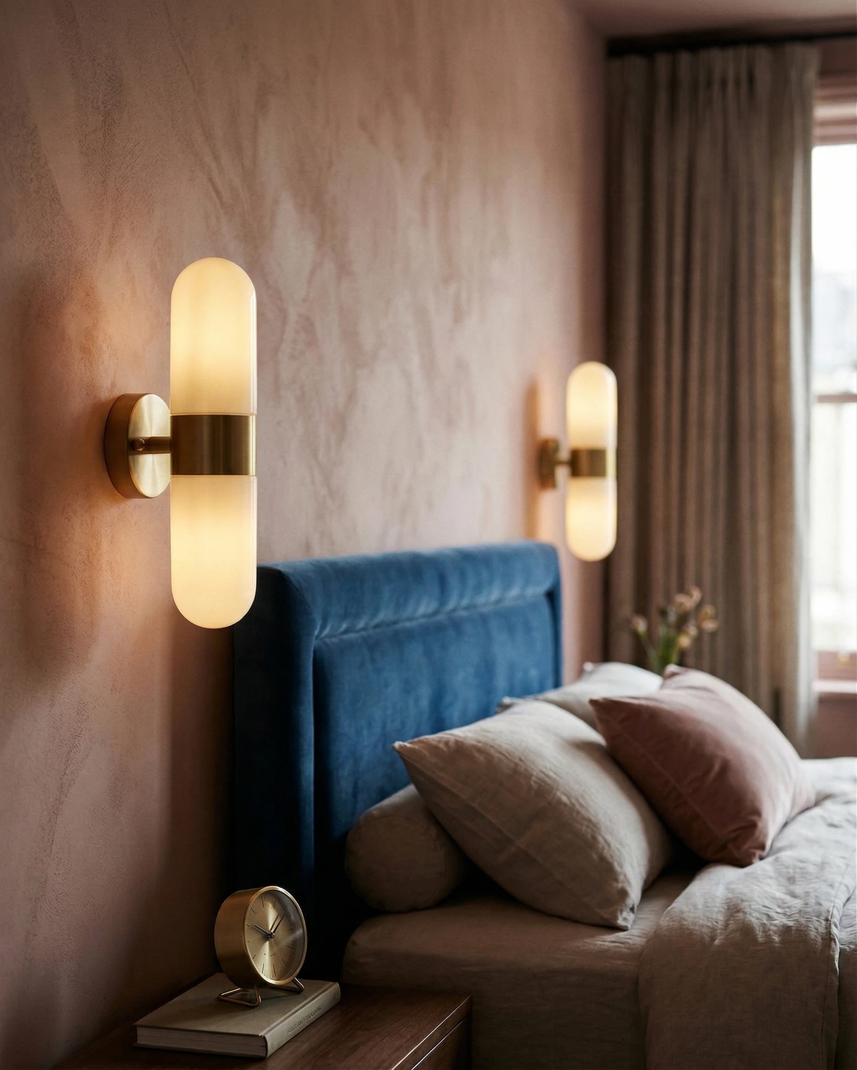 Brass wall sconce COMETA No.01 in brushed brass switched on either side of a navy velvet headboard