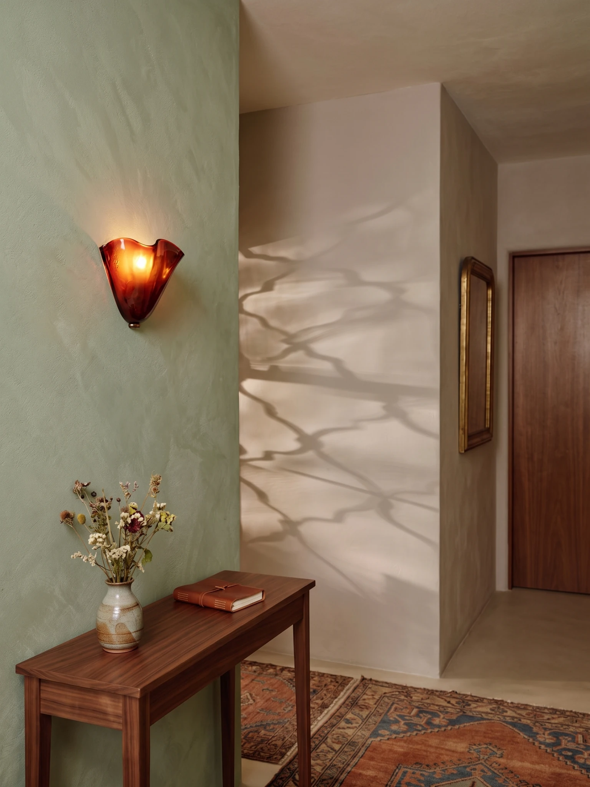 Brass wall sconce DALIA No.03 with amber glass switched on above a wood console table on a sage green wall