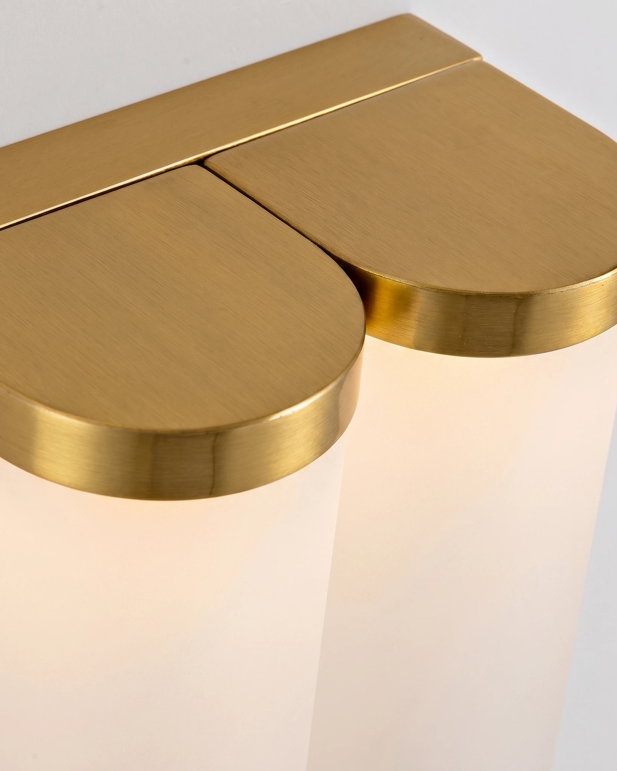 Close-up of the two antique brass caps over the frosted glass shields of the PILA No.01 brass wall sconce