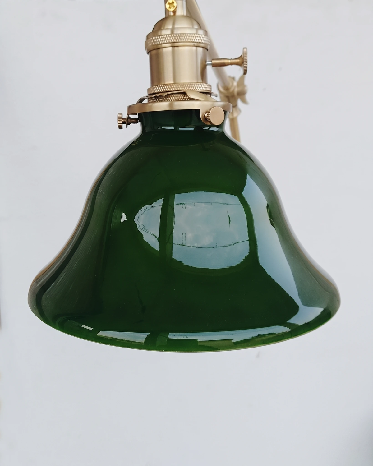 Close-up of the dark emerald glass bell shade of the DALIA No.04 brass wall sconce with its brass fitting
