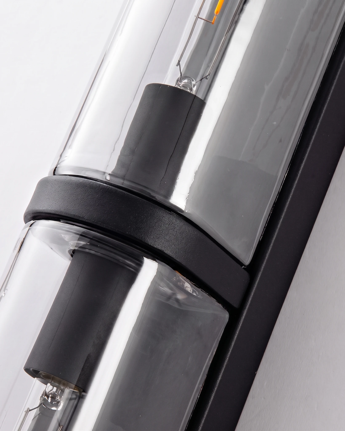Close-up of the smoked glass column and matte black iron band of the PILA No.01 brass wall sconce with bulb inside