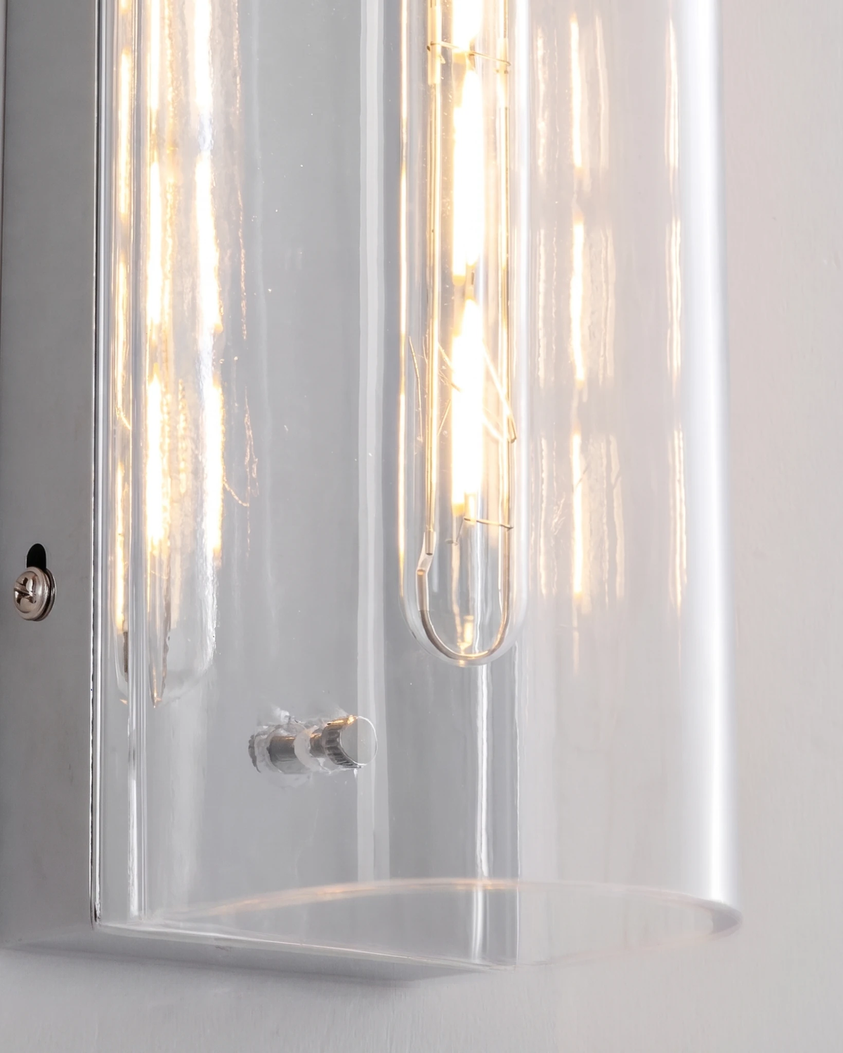 Close-up of the clear glass shield and glowing filament bulbs of the PILA No.01 brass wall sconce with chrome screw