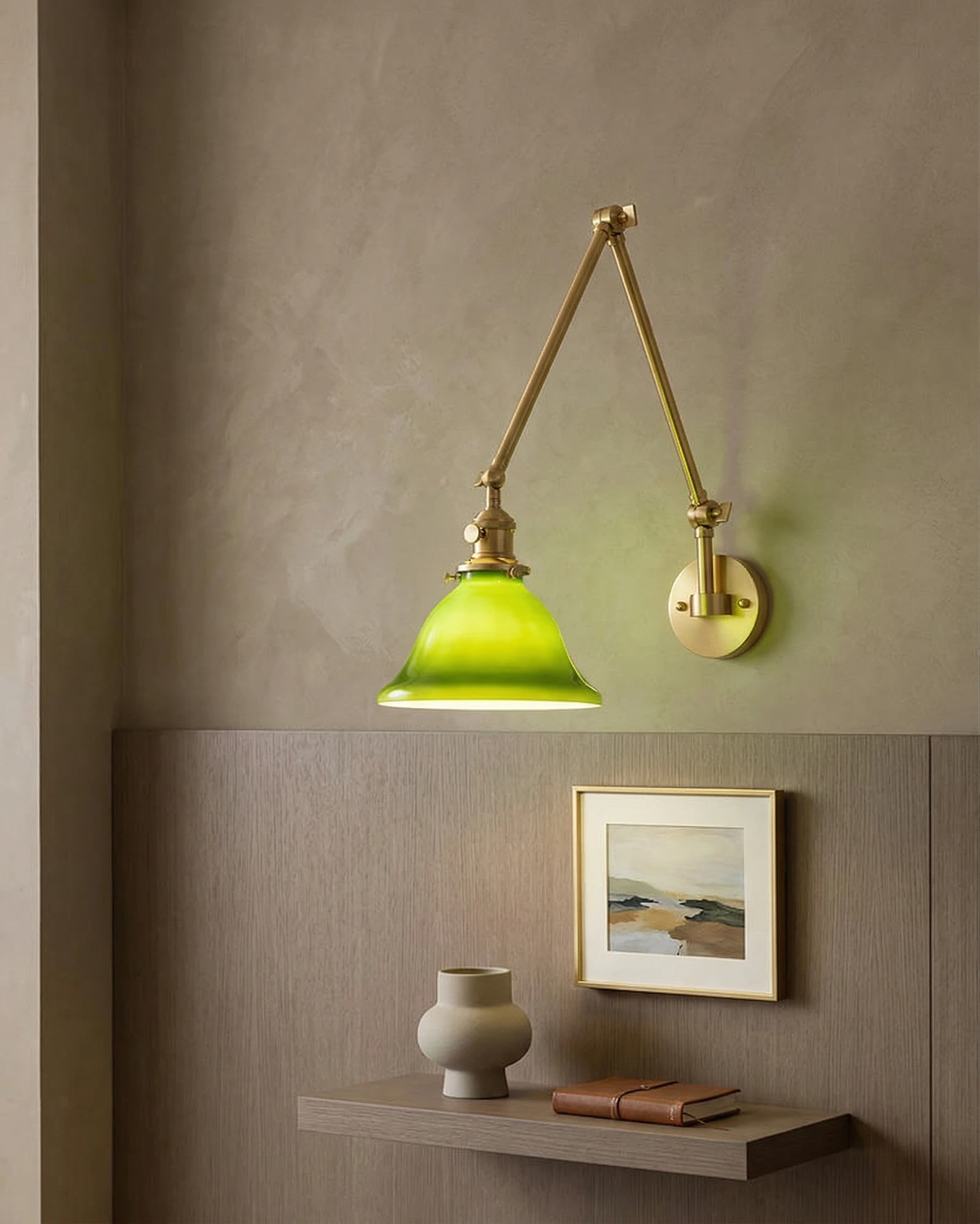 Brass wall sconce DALIA No.04 with extending arm, lit on a plaster wall above a shelf with a framed print