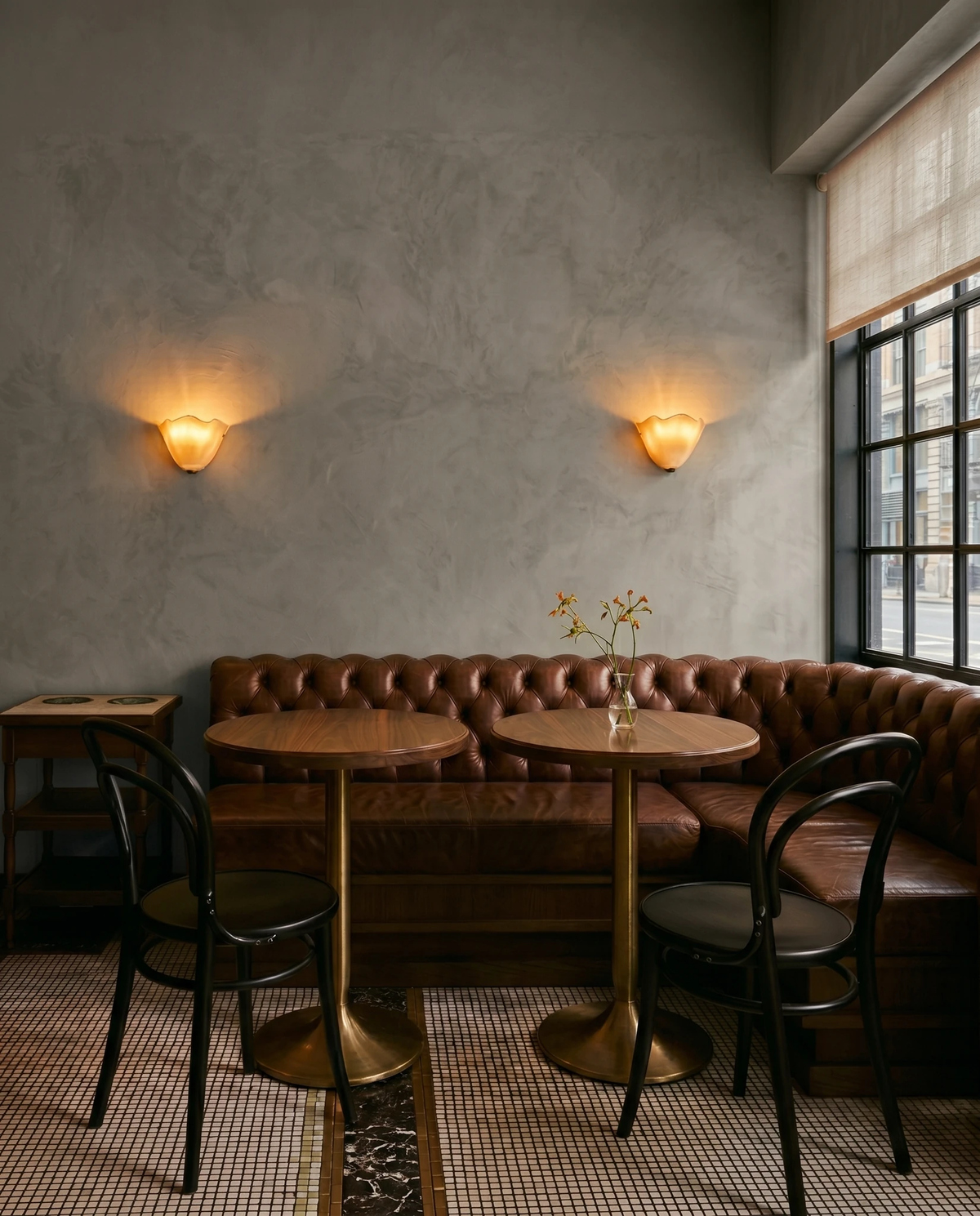 Two brass wall sconces DALIA No.03 in amber glass lit above leather banquettes and round tables in a restaurant