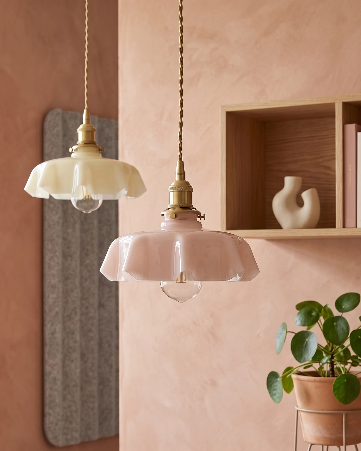 Two ceramic pendant lights CORA No.01 in sand and dusty rose lit against a terracotta plaster wall with a shelf niche