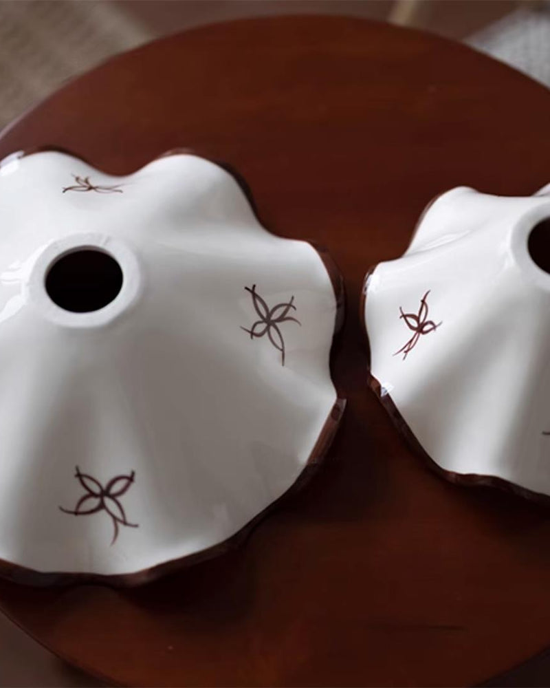 Close-up of two CAPRI No.01 ceramic pendant light shades laid on a dark red table showing the painted flowers and cord holes
