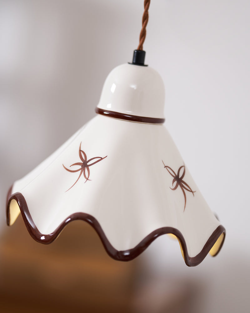 Close-up of the CAPRI No.01 ceramic pendant light lit from inside, bell top, twisted cord and brown wavy rim