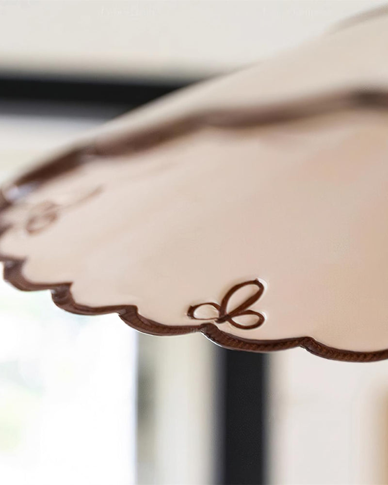 Close-up of the scalloped edge and bow detail of the ceramic pendant light MELI No.04 by a window