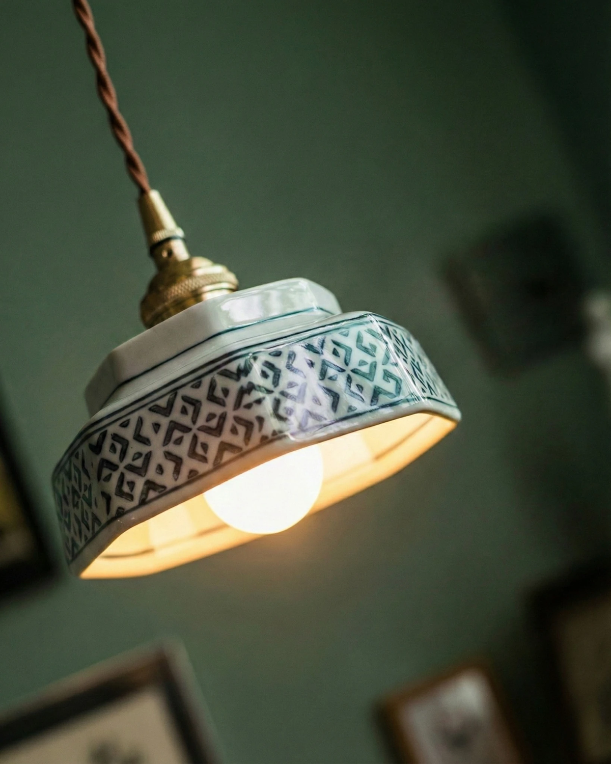 Close-up of the ceramic pendant light RAGUSA No.02 shade with its jade geometric pattern and lit bulb on a green wall