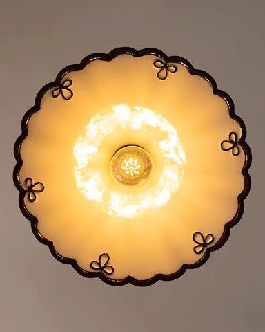 Close-up from below of the lit MELI No.02 ceramic pendant light showing the scalloped brown-edged rim