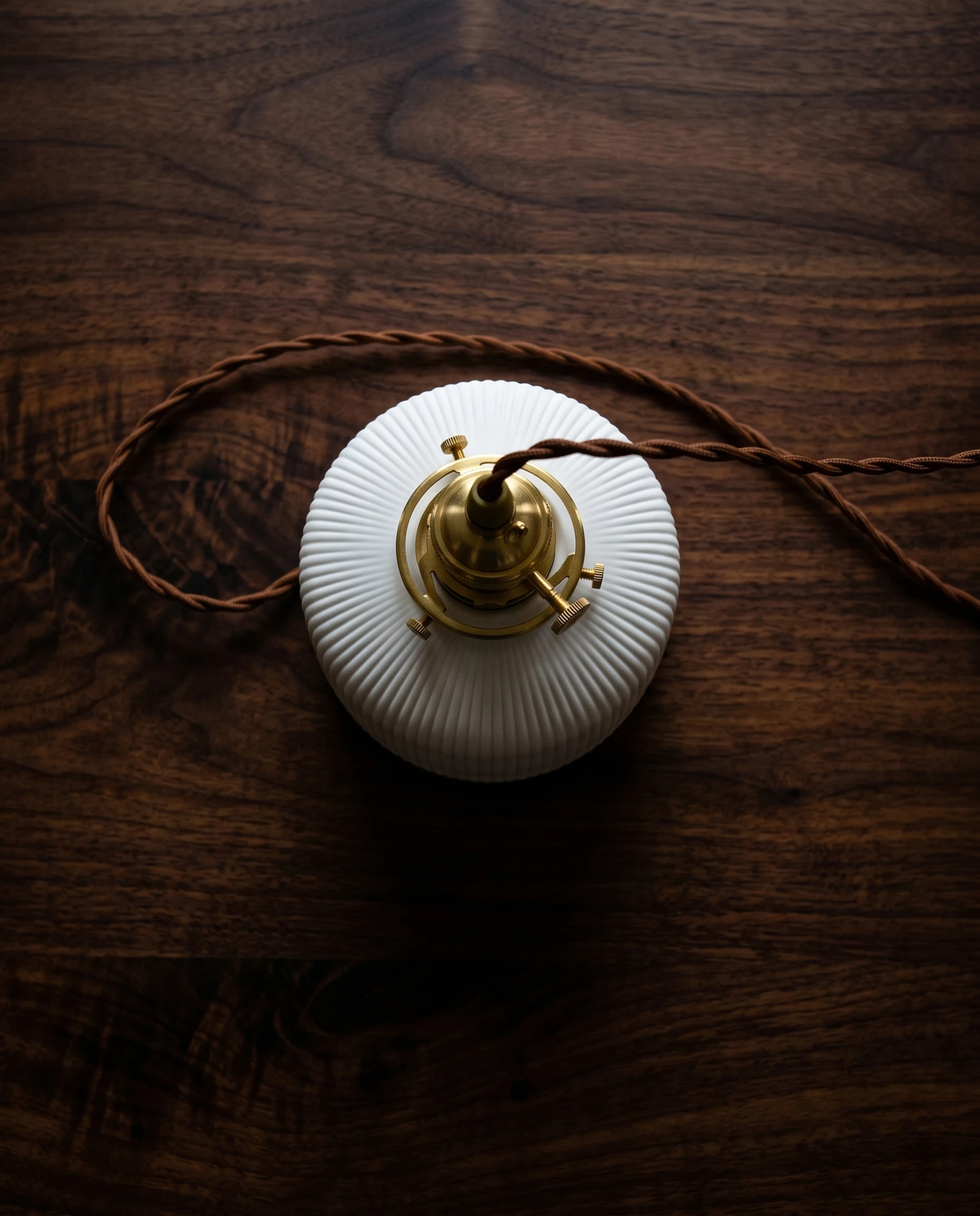 Close-up of the SERA No.01 ceramic pendant light seen from above, brass socket and twisted brown cord on a walnut surface