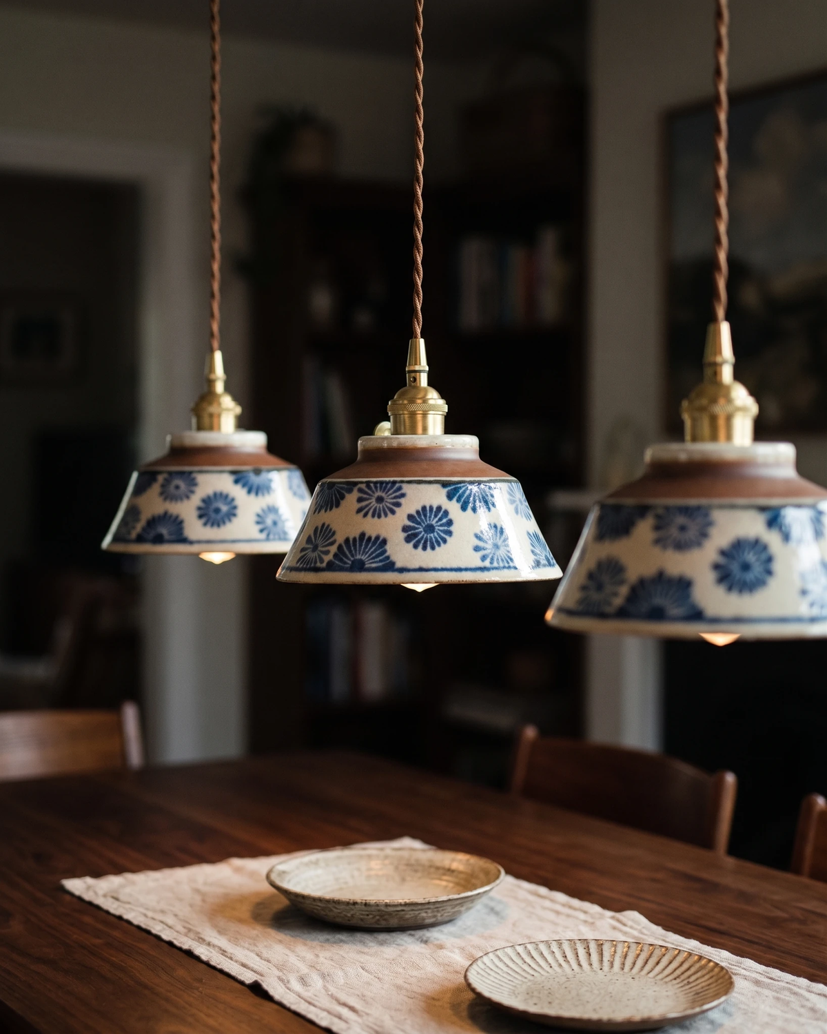 Three ceramic pendant lights MELI No.05 in indigo floral lit in a row above a dark wood dining table
