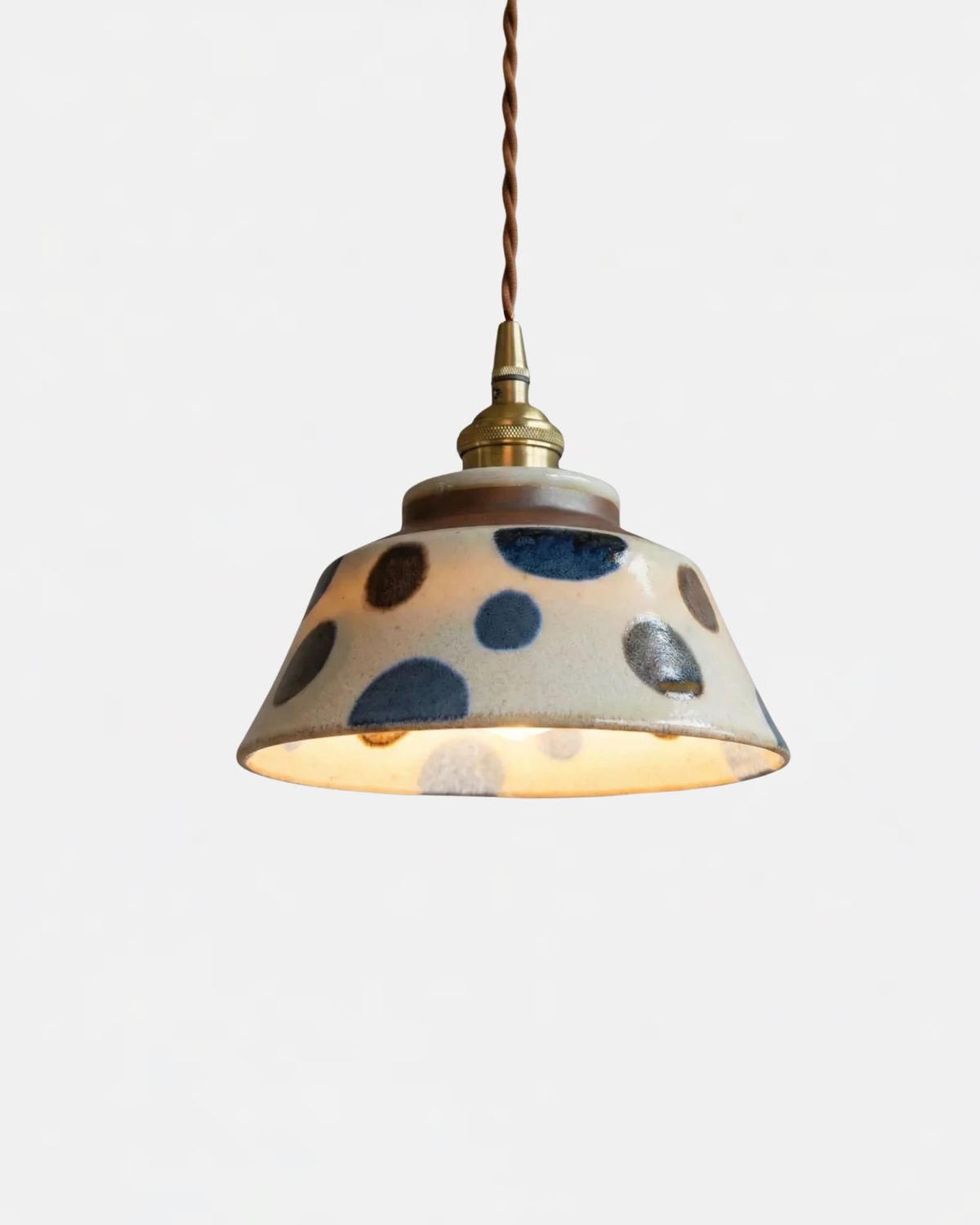 Ceramic pendant light MELI No.05 in Ocean Splash, blue splashes on a white bell hung from a twisted cord, lit