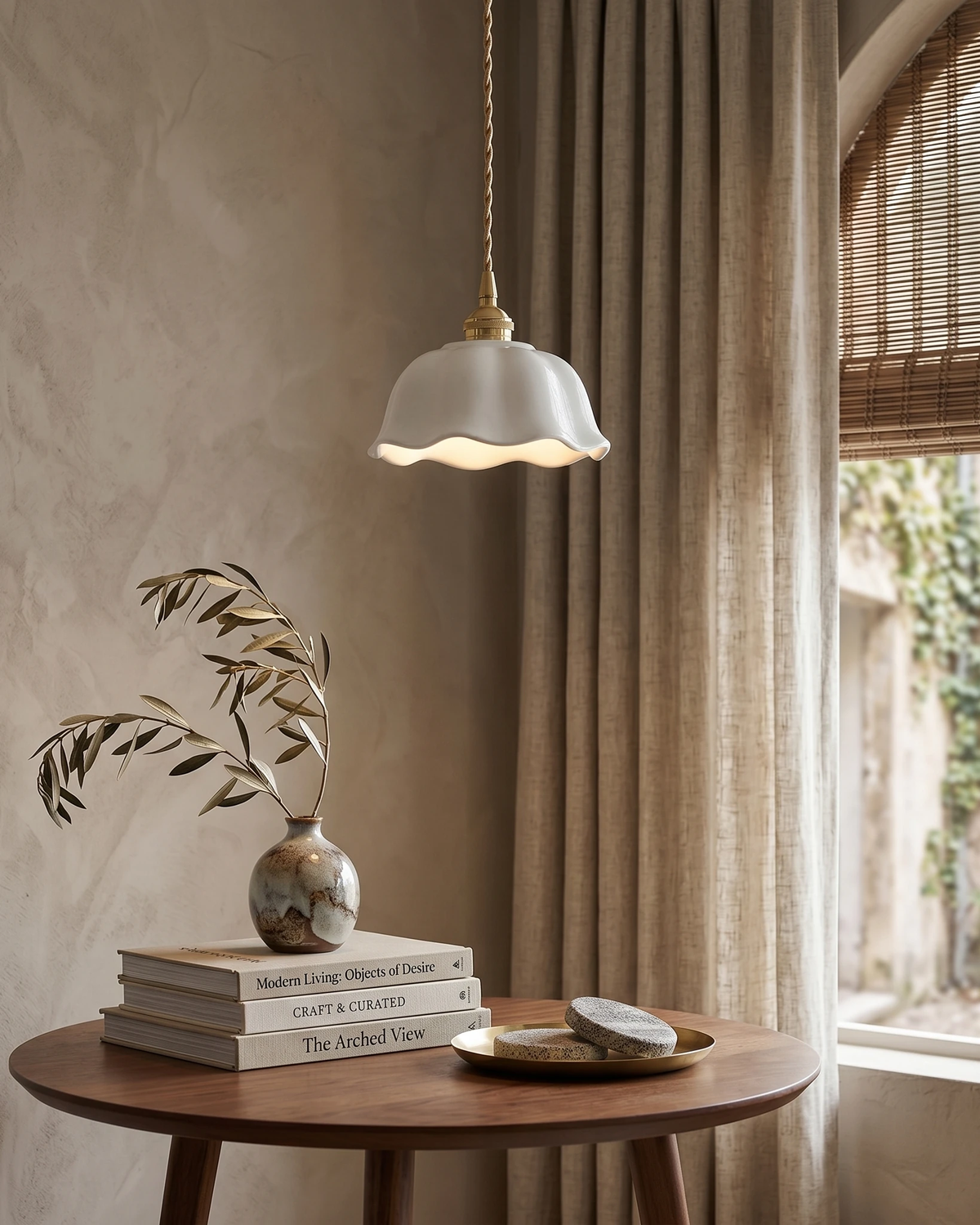 Ceramic pendant light MELI No.03 lit above a round walnut side table with books and a vase of olive branches