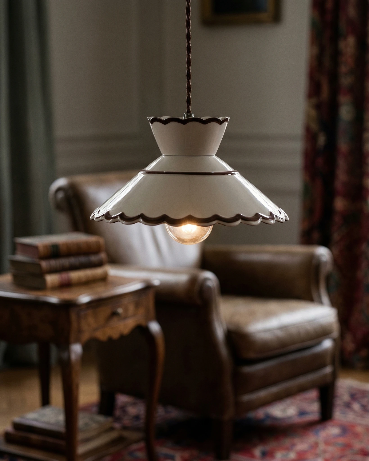 Ceramic pendant light MELI No.04 lit above a leather armchair and side table with books in a reading nook