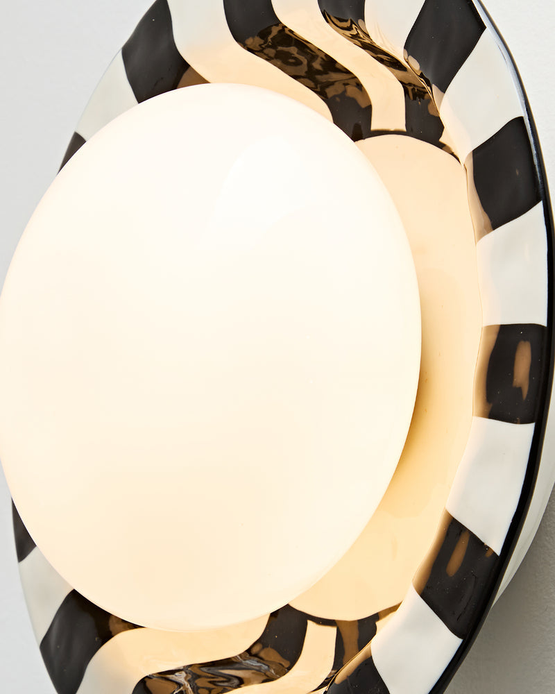 Close-up of the ceramic wall sconce OLEA No.01 showing the lit opal globe and hand-striped black and white rim