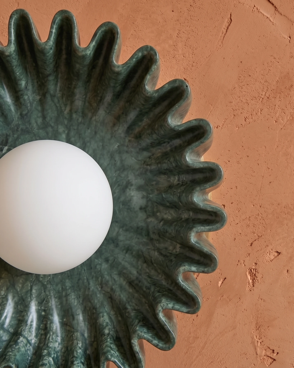 Close-up of the RAGGI No.01 ceramic wall sconce in green with an unlit white globe against a terracotta wall