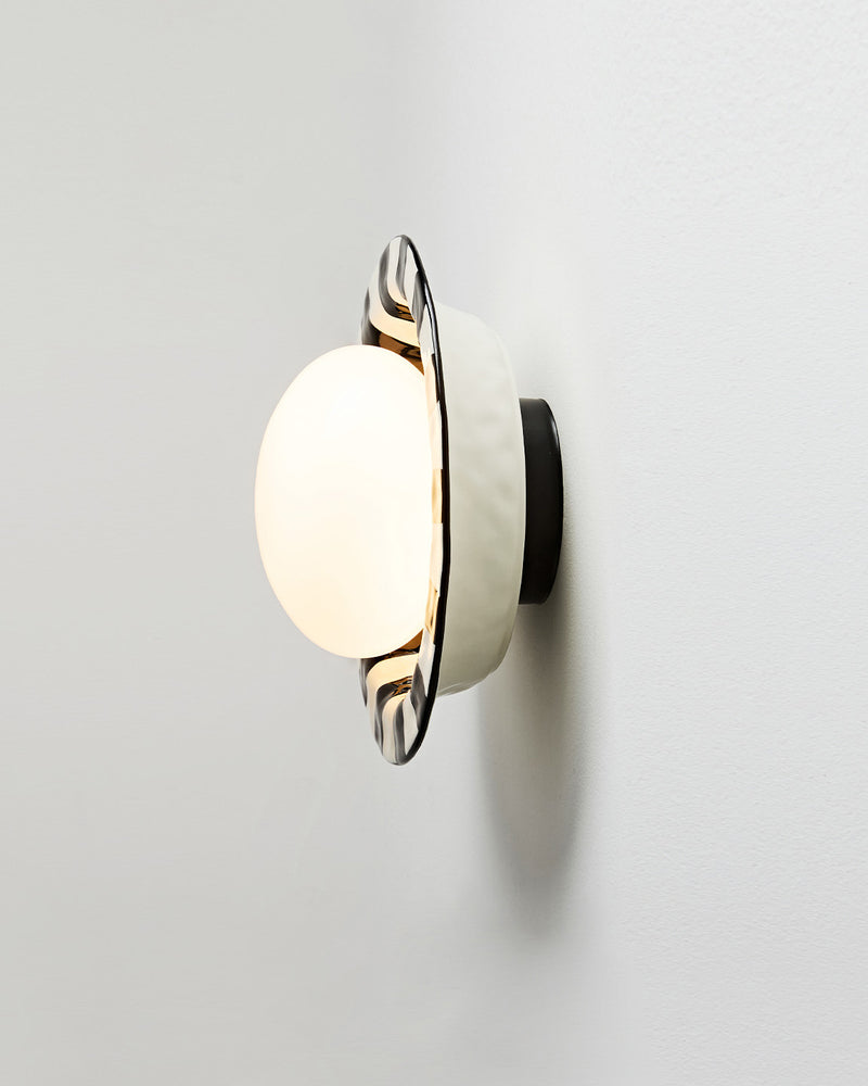 Ceramic wall sconce OLEA No.01 seen from the side, opal globe lit in front of the black and white striped corolla