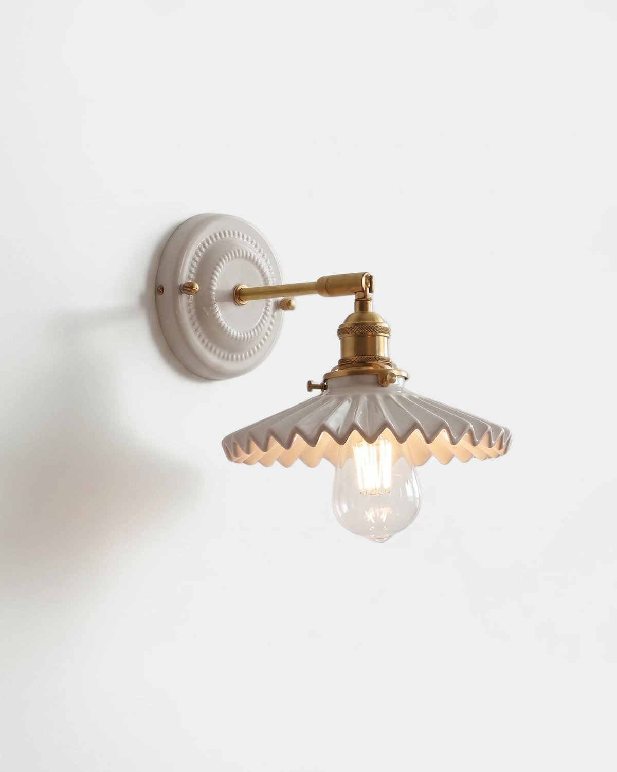 Ceramic wall sconce RIGA No.03, white pleated umbrella shade on a brass swing arm with the bulb lit