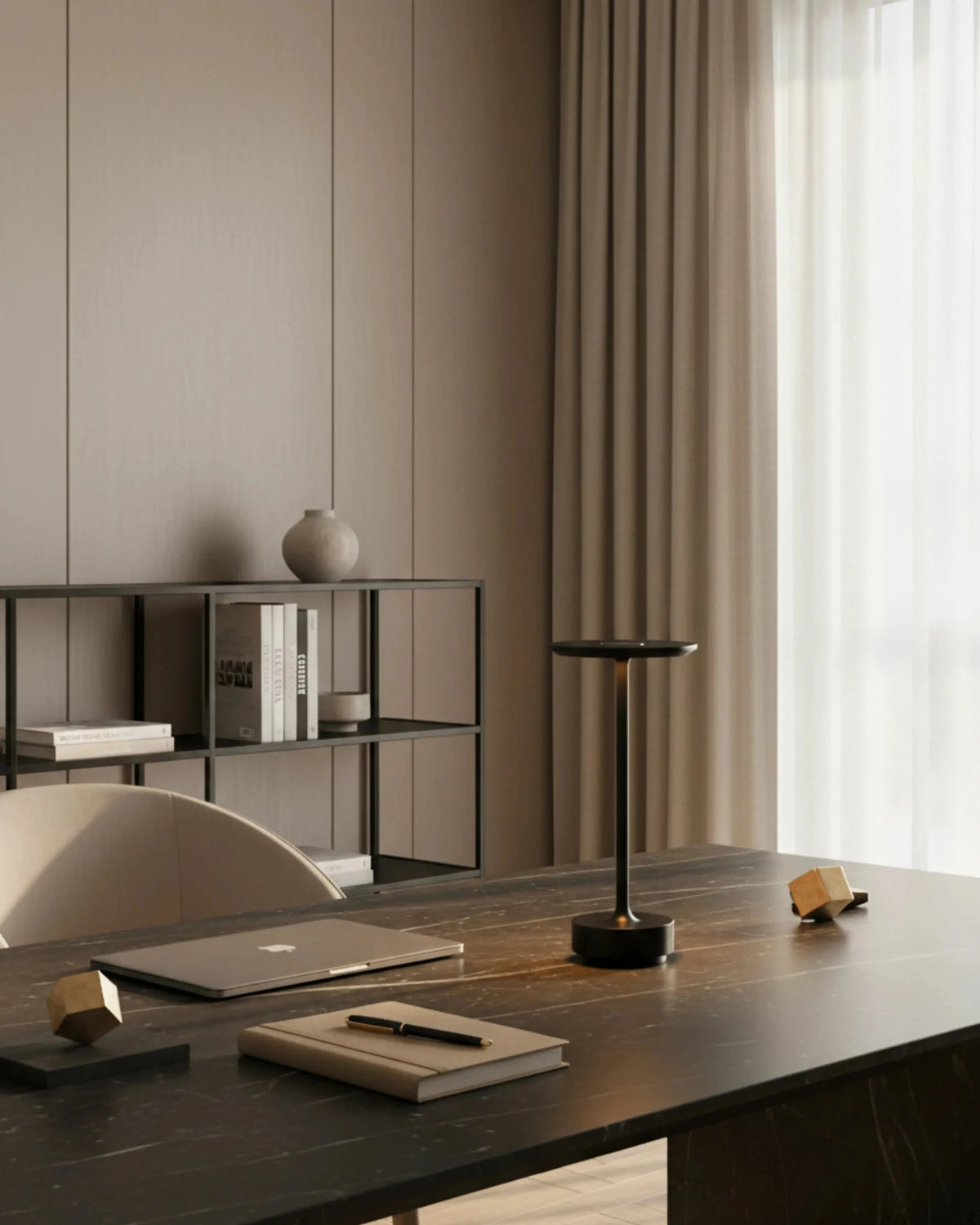 Cordless desk lamp LUMA No.05 in black lit on a dark wood desk with a laptop and notebook, shelving behind