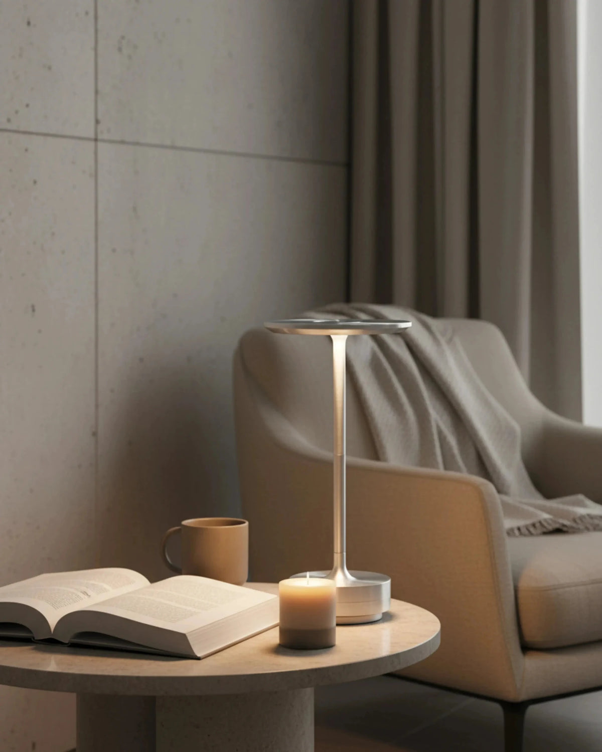 Cordless desk lamp LUMA No.05 in silver lit on a round side table with an open book beside an armchair